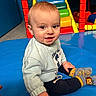 baby, child, smiling, sitting, indoor, playground, colorful, clothing, sock, face, person, toy, play_area, happy, cute, young_child, sweatshirt, floor_mat, bright, portrait