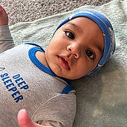 Elijah is registered to the contest to win money with this photo: baby, blanket, blue, carpet, child, closeup, clothing, cute, expression, eyes, face, grey, hand, hat, indoors, infant, lying_down, onesie, portrait, soft_texture
