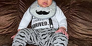 Elijah is registered to the contest to win money with this photo: baby, bib, brown_couch, casual, child, clothing, couch, cute, hat, indoor, infant, looking_at_camera, mustache_pattern, pants, person, portrait, sitting, socks, wide_eyes, young_child