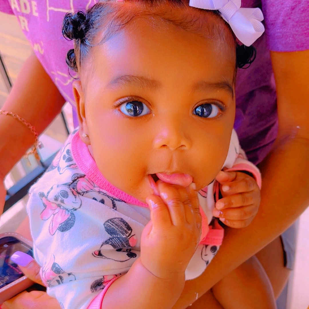 Ahnesti joined the competition — help win amazing prizes! baby, child, infant, person, holding, pink_bow, white_bow, onesie, cartoon_print, purple_shirt, hands, fingers, mouth, cute, adorable, indoor, closeup, face, smiling, big_eyes