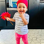 Maya a rejoint le concours — aidez-le/la à gagner de superbes lots ! toddler, child, red_bandana, flower, pink_pants, striped_shirt, barefoot, indoor, kitchen, rug, oven, cabinet, smiling, playful, person, standing, hand, finger, cute, home