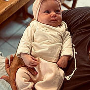 Maëlya a rejoint le concours — aidez-le/la à gagner de superbes lots ! baby, infant, child, person, headband, clothing, hand, arm, table, wood, fabric, sitting, indoor, cute, soft_colors, portrait, looking_away, cozy, nurturing, family