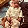 baby, infant, child, person, headband, clothing, hand, arm, table, wood, fabric, sitting, indoor, cute, soft_colors, portrait, looking_away, cozy, nurturing, family
