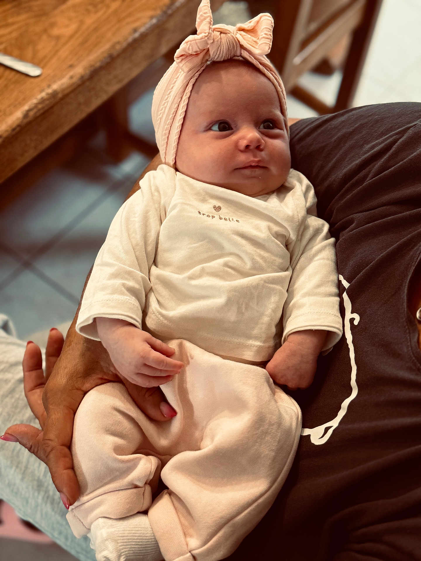 Maëlya a rejoint le concours — aidez-le/la à gagner de superbes lots ! baby, infant, child, person, headband, clothing, hand, arm, table, wood, fabric, sitting, indoor, cute, soft_colors, portrait, looking_away, cozy, nurturing, family
