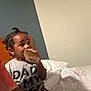 Nolan is registered to the contest to win money with this photo: child, sandwich, bed, pigtails, shirt, text, indoor, person, eating, food, casual, young_child, hair, head, face, clothing, furniture, blanket, relaxed, home