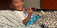 Nolan joined the competition — help win amazing prizes! toddler, smiling, bed, blanket, food, remote_control, television, dresser, living_room, kitchen, child, person, indoor, happy, hair, clothing, furniture, pattern, plate, footwear