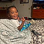 toddler, smiling, bed, blanket, food, remote_control, television, dresser, living_room, kitchen, child, person, indoor, happy, hair, clothing, furniture, pattern, plate, footwear