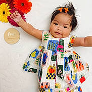 Gianna is registered to the contest to win money with this photo: baby, child, infant, colorful_dress, flowers, gerbera_daisies, wooden_plaque, four_months, smiling, cute, lying_down, hair_clips, white_background, patterned_clothing, happy, portrait, young_child, outstretched_arms, indoor, playful