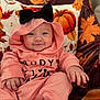 autumn, baby, black_bow, blanket, child, clothing, cozy, cute, face, happy, hoodie, indoors, infant, leaf_pattern, pink_clothing, portrait, pumpkin, sitting, smile, soft