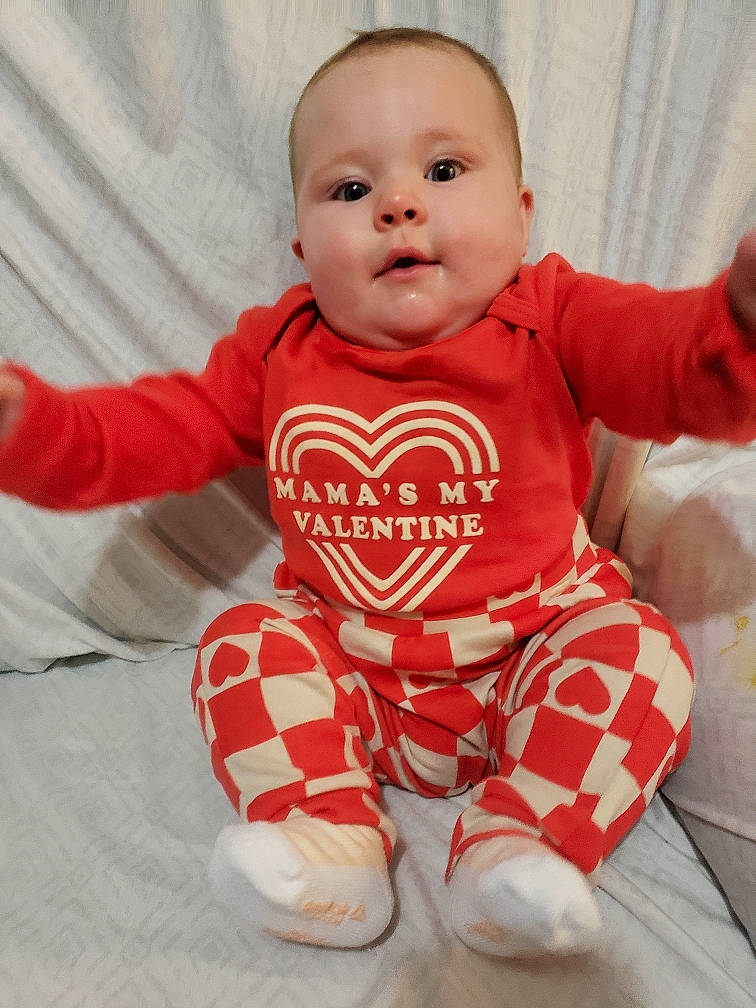Montana is registered to the contest to win money with this photo: baby, baby_toddler_clothing, carmine, cheek, child, comfort, floor, flooring, happy, human_body, leg, long_sleeved_t_shirt, nose, pattern, person, sitting, sleeve, smile, t_shirt, textile