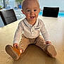 baby, child, smiling, happy, table, wooden_table, indoor, window, pool, pants, shirt, footwear, brown_shoes, person, face, seated, home, daylight, plant, background