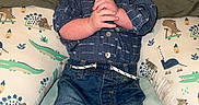 Jaxson is registered to the contest to win money with this photo: baby, child, infant, clothing, jeans, shirt, socks, pillow, dinosaur_pattern, bed, blanket, hands, face, portrait, indoor, cute, smile, person, young, comfortable