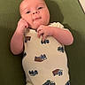 baby, infant, onesie, clothing, green_background, lying_down, cute, child, face, portrait, small_hands, truck_pattern, fabric, indoors, skin, head, eyes, furniture, baby_garment, newborn