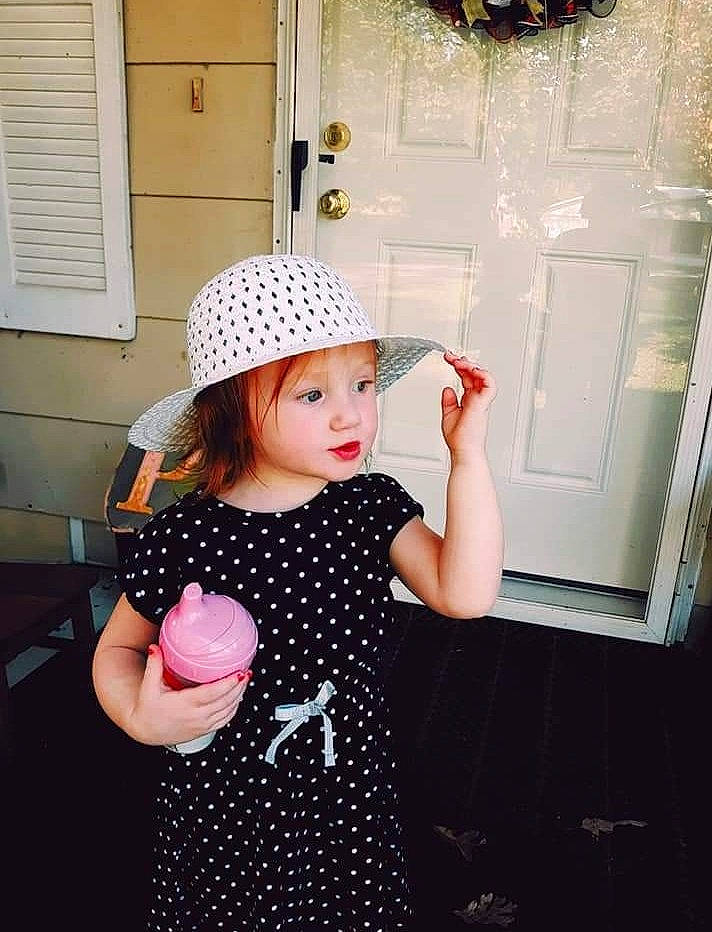 Talia is registered to the contest to win money with this photo: arm, baby_toddler_clothing, cap, dress, gesture, happy, hat, headgear, headwear, joint, neck, pattern, person, photograph, shoulder, sleeve, standing, street_fashion, textile, toddler