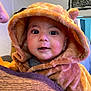baby, child, hoodie, fuzzy_clothing, face, person, indoor, portrait, cute, warm_clothing, smile, eyes, headwear, adult, holding, cozy, expression, furniture, wall, decor