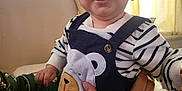 Qasim is registered to the contest to win money with this photo: baby, smiling, child, face, striped_clothing, bear_patch, hand, person, indoor, curtains, window_light, holding, happy, cute, toddler, apparel, portrait, skin, sitting, fabric