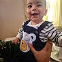 baby, smiling, child, face, striped_clothing, bear_patch, hand, person, indoor, curtains, window_light, holding, happy, cute, toddler, apparel, portrait, skin, sitting, fabric