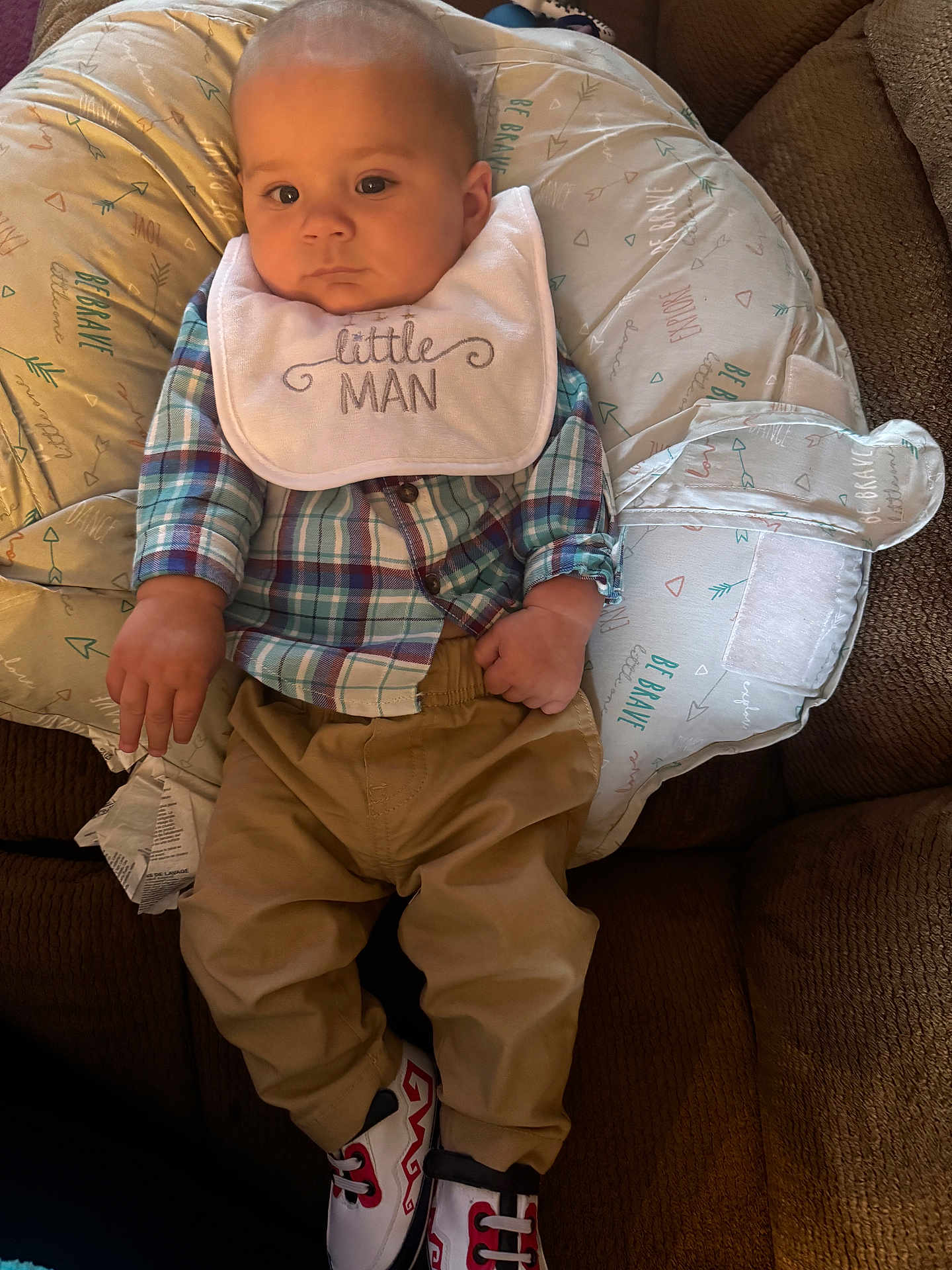 Kace Ray Lewis joined the competition — help win amazing prizes! baby, child, plaid_shirt, bib, khaki_pants, sneakers, couch, pillow, infant, face, hands, clothing, indoor, person, young_child, cute, seated, text_on_bib, footwear, relaxed