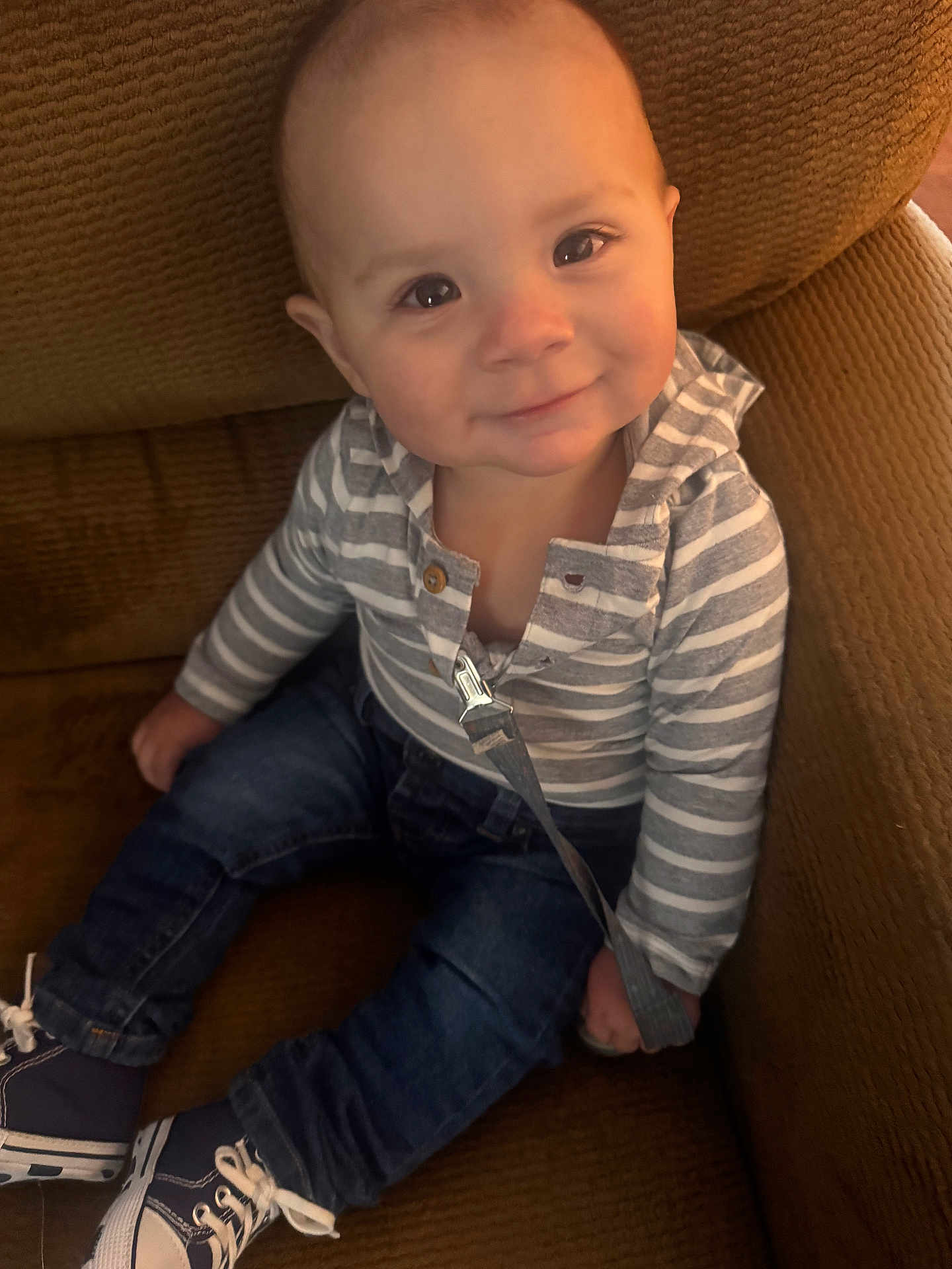 Kace is registered to the contest to win money with this photo: baby, child, smiling, striped_hoodie, denim_jeans, sneakers, seated, brown_chair, indoors, cute, face, portrait, young_child, happy, casual_clothing, person, candid, cozy, small_shoes, infant