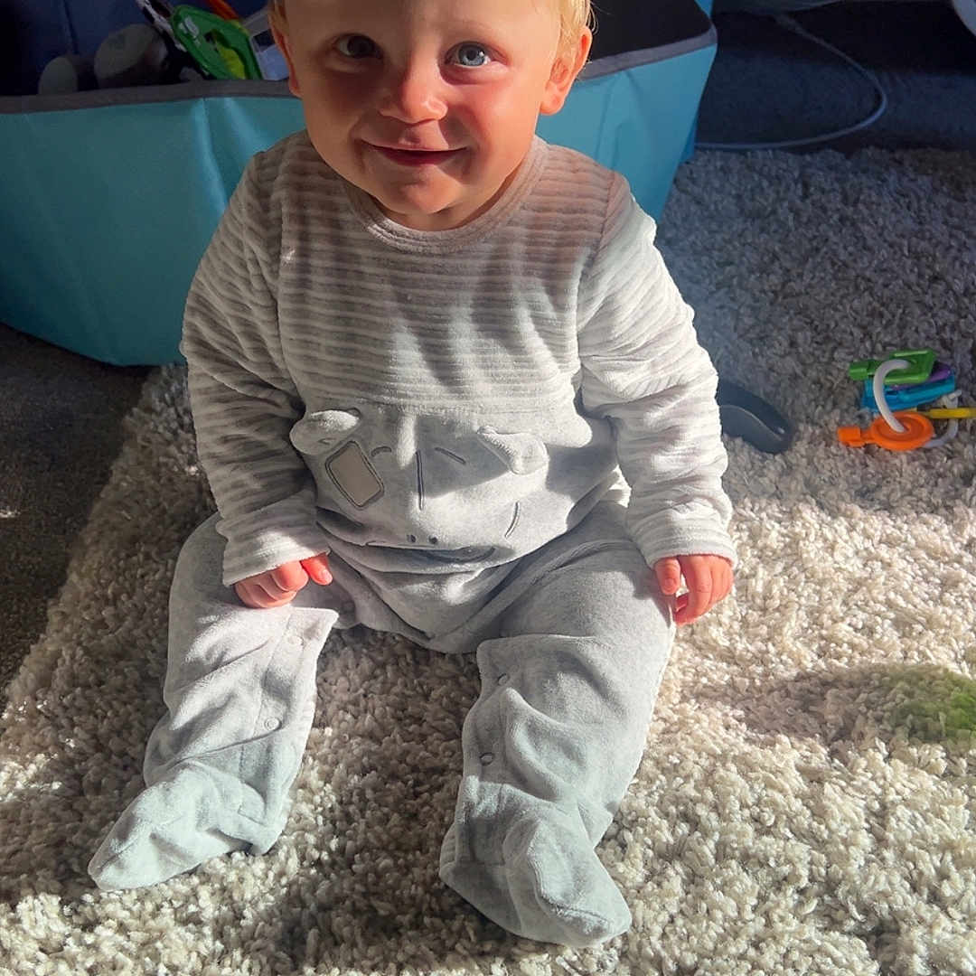 Lucas joined the competition — help win amazing prizes! baby, blond_hair, blue_eyes, carpet, child, clothing, cute, floor, happy, indoor, infant, onesie, playpen, room, shadow, sitting, smile, sunlight, toddler, toy