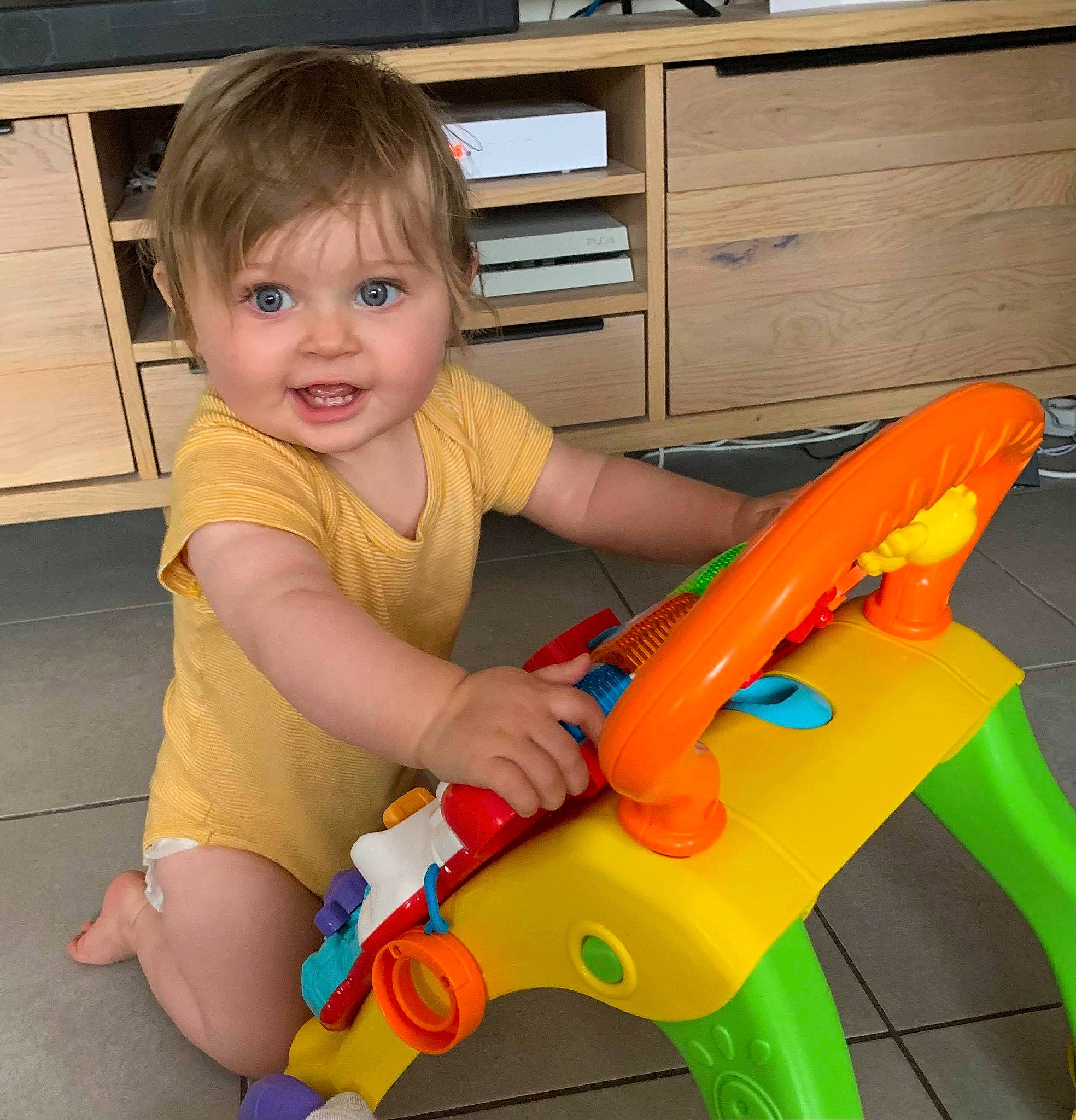 Lola participe au concours pour gagner de l'argent avec cette photo : baby_playing_with_toys, baby_toddler_clothing, cabinetry, child, drawer, fun, hair, human_leg, lap, leisure, musical_instrument, person, plastic, play, riding_toy, sitting, smile, thigh, toddler, toy
