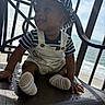 baby, child, smiling, hat, striped_clothing, overalls, socks, chair, balcony, ocean, sky, sunlight, happy, portrait, outdoor, nautical, infant, seat, person, daytime