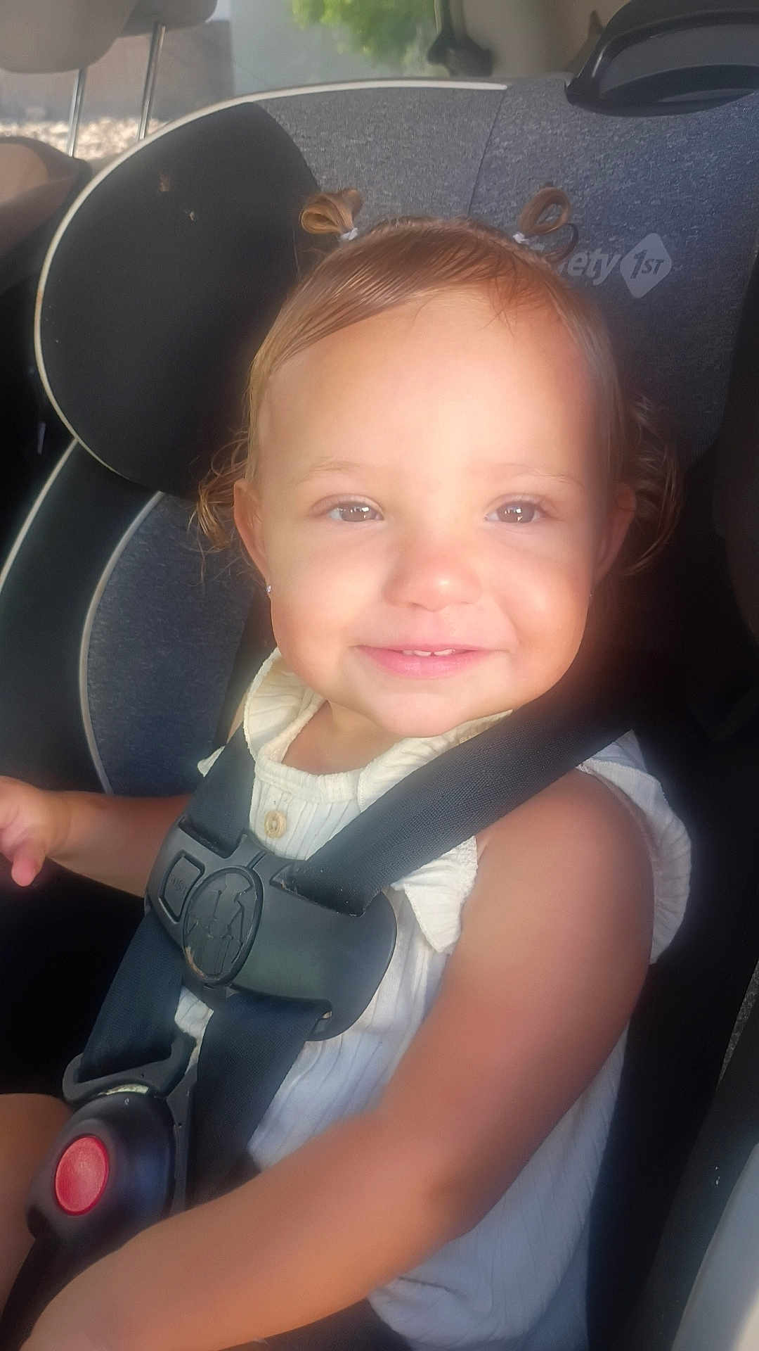 Emelina joined the competition — help win amazing prizes! child, toddler, car_seat, safety_harness, smile, hair_ties, cute, seatbelt, infant, baby, face, portrait, young_child, sunlight, indoors, clothing, white_top, happy, person, car_interior