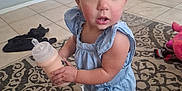 Emelina is registered to the contest to win money with this photo: toddler, child, baby_bottle, indoor, carpet, barefoot, curly_hair, blue_outfit, standing, expression, toy, floor_tiles, furniture, person, home, patterned_rug, casual, curious, small_ponytail, holding