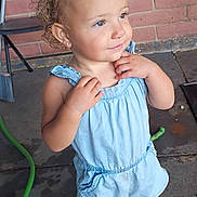 Emelina joined the competition — help win amazing prizes! toddler, child, cute, curly_hair, blue_bow, romper, white_shoes, standing, brick_wall, concrete_floor, chair, earrings, curious_expression, indoors, person, young_child, casual_clothing, footwear, hair_style, portrait