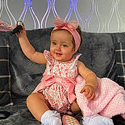 Lottie joined the competition — help win amazing prizes! baby, child, girl, pink_bow, headband, floral_outfit, socks, blanket, toy_phone, keys, couch, gray_couch, smiling, happy, indoor, wallpaper, plush_blanket, cute, seated, home