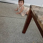 Karla is registered to the contest to win money with this photo: carpet, child, crawling, cute, dress, floor, furniture, happy, home, indoor, marble_table, person, plush_toy, power_outlet, smiling, table_leg, toddler, toy, wall, yellow_string