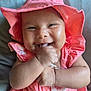baby, infant, child, smiling, happy, cute, pink_hat, pink_dress, hand, face, skin, indoors, portrait, closeup, young_child, cheeks, sitting, cushion, bright_colors, joy