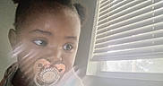 Imani is registered to the contest to win money with this photo: baby, blinds, casual, child, closeup, curious, expression, face, hair_buns, indoor, light, natural_light, pacifier, person, portrait, skin, soft_light, toddler, window, young_child