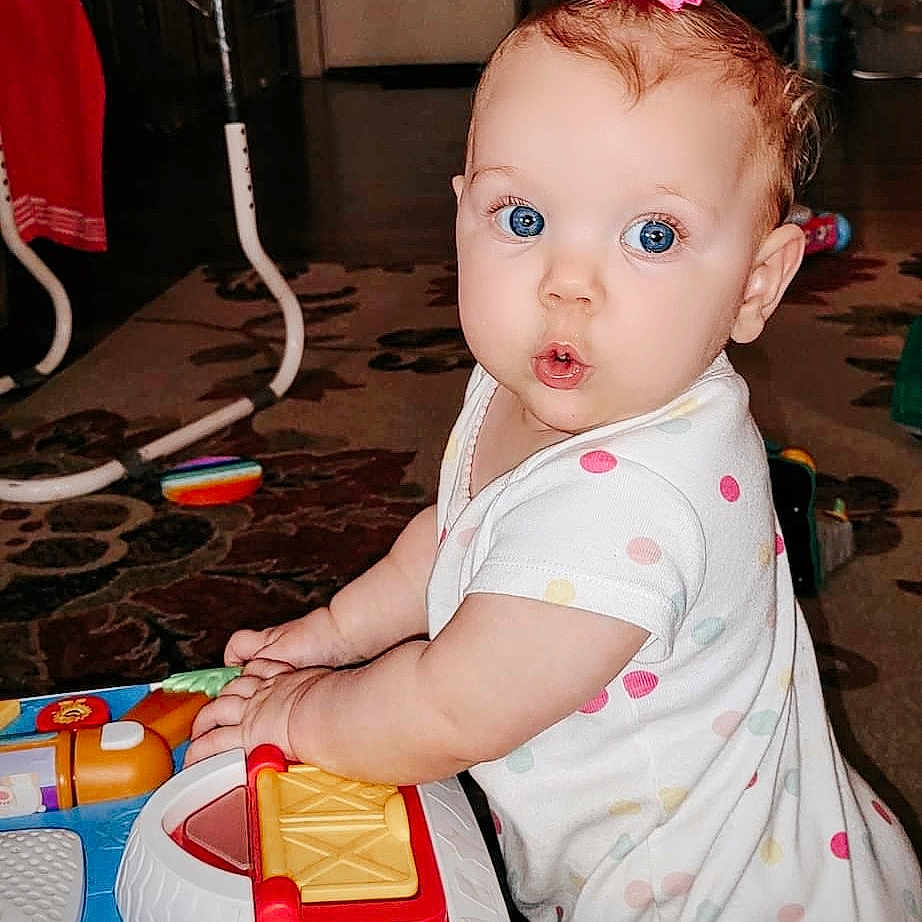 Anndrea joined the competition — help win amazing prizes! baby, carpet, child, colorful, curiosity, expression, face, floor, furniture, hands, home, indoor, light, person, pink_bow, playing, polka_dot, toy, white_clothing, young_child