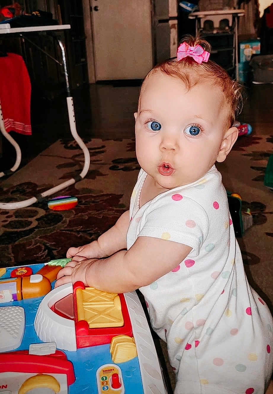 Anndrea joined the competition — help win amazing prizes! baby, child, indoor, toy, playing, polka_dot, white_clothing, pink_bow, carpet, furniture, face, hands, expression, person, colorful, floor, curiosity, young_child, home, light