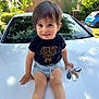 black_shirt, car, casual_clothing, child, cute, daylight, face, greenery, happy, keys, outdoor, portrait, shorts, sitting, smiling, sunlight, toddler, trees, white_car, young_child