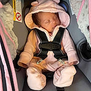 Leilani is registered to the contest to win money with this photo: baby, blanket, car_seat, child, cozy, cute, face, headwear, hood, indoors, infant, newborn, onesie, peaceful, pink_clothing, seatbelt, sleeping, soft_texture, straps, toddler