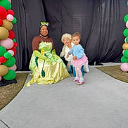 Mavis joined the competition — help win amazing prizes! balloon_arch, child, toddler, princess_costume, roller_skates, balloons, costume_party, smiling, outdoor, concrete_path, black_backdrop, green_gloves, yellow_dress, pink_tutu, curly_hair, happy, people, event, celebration, colorful