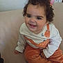 Rahma a rejoint le concours — aidez-le/la à gagner de superbes lots ! toddler, child, smiling, curly_hair, pink_hair_clip, dinosaur_outfit, orange_pants, beige_couch, happy, indoors, cute, person, baby, sitting, portrait, clothing, face, hand, young_child, cozy