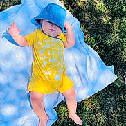 David a rejoint le concours — aidez-le/la à gagner de superbes lots ! baby, blanket, blue_hat, casual_clothing, child, feet, grass, greenery, infant, lying_down, nature, one_person, outdoor, person, relaxing, skin, summer, sunlight, sunny, yellow_clothing