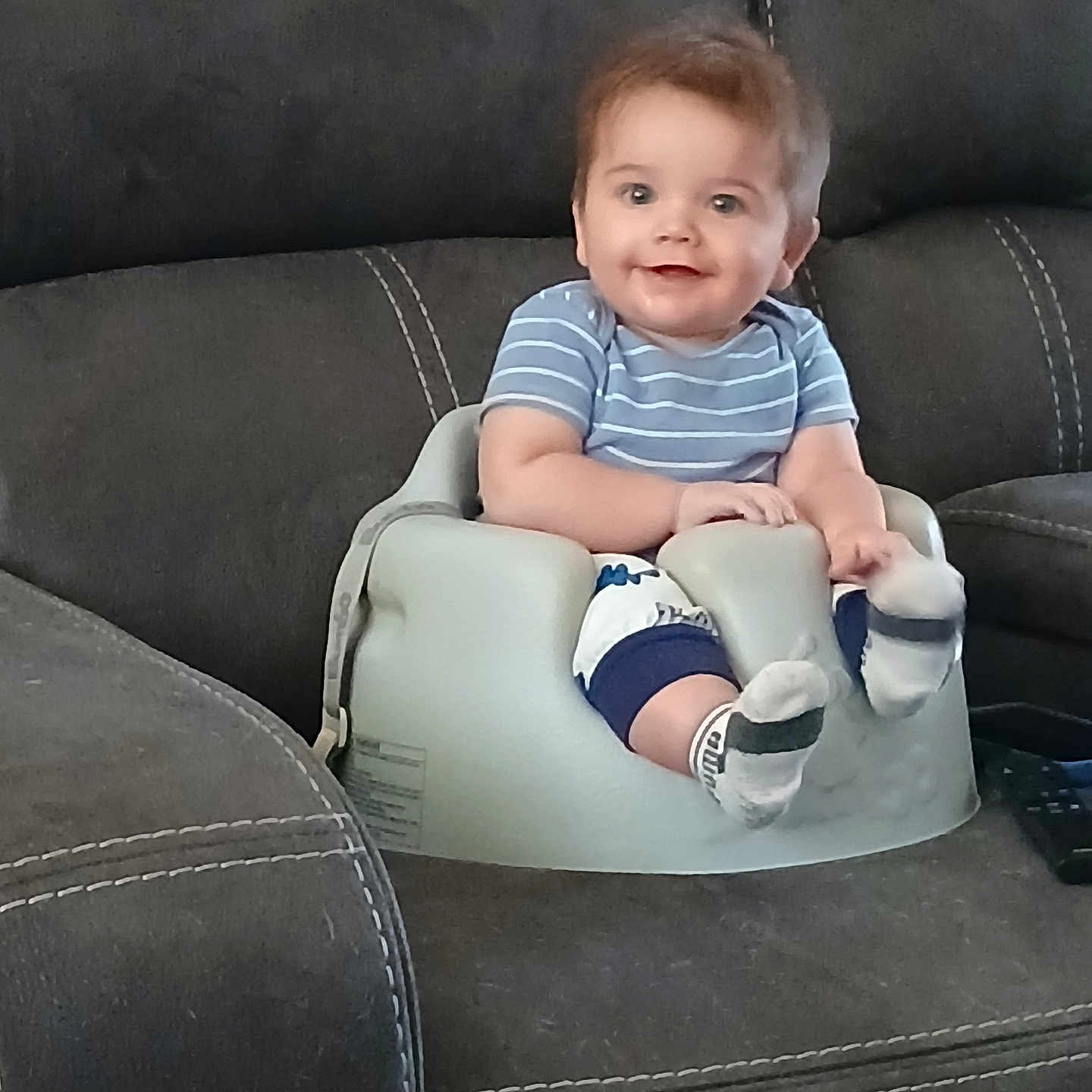 Luke James joined the competition — help win amazing prizes! baby, baby_seat, child, clothing, couch, cute, face, furniture, happy, indoor, infant, living_room, pants, person, sitting, smiling, socks, sofa, striped_shirt, young
