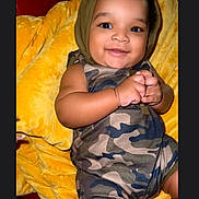 Jett is registered to the contest to win money with this photo: baby, child, smiling, camouflage, clothing, blanket, yellow, hood, cute, face, portrait, happy, infant, sitting, indoors, skin, hand, legs, couch, comfortable