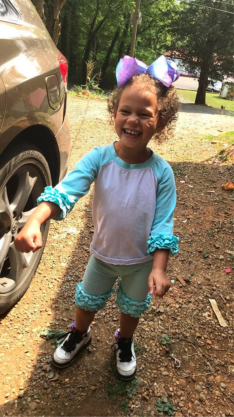 Zayla is registered to the contest to win money with this photo: asphalt, automotive_tire, bumper, car, fender, fun, grass, happy, joy, leisure, motor_vehicle, people, person, pink, plant, shorts, smile, tire, tree, vehicle