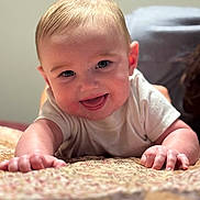 Tate is registered to the contest to win money with this photo: baby, smiling, infant, face, hands, blanket, pattern, happy, cute, person, skin, closeup, portrait, indoors, toddler, crawling, young_child, soft_light, expression, casual_clothing