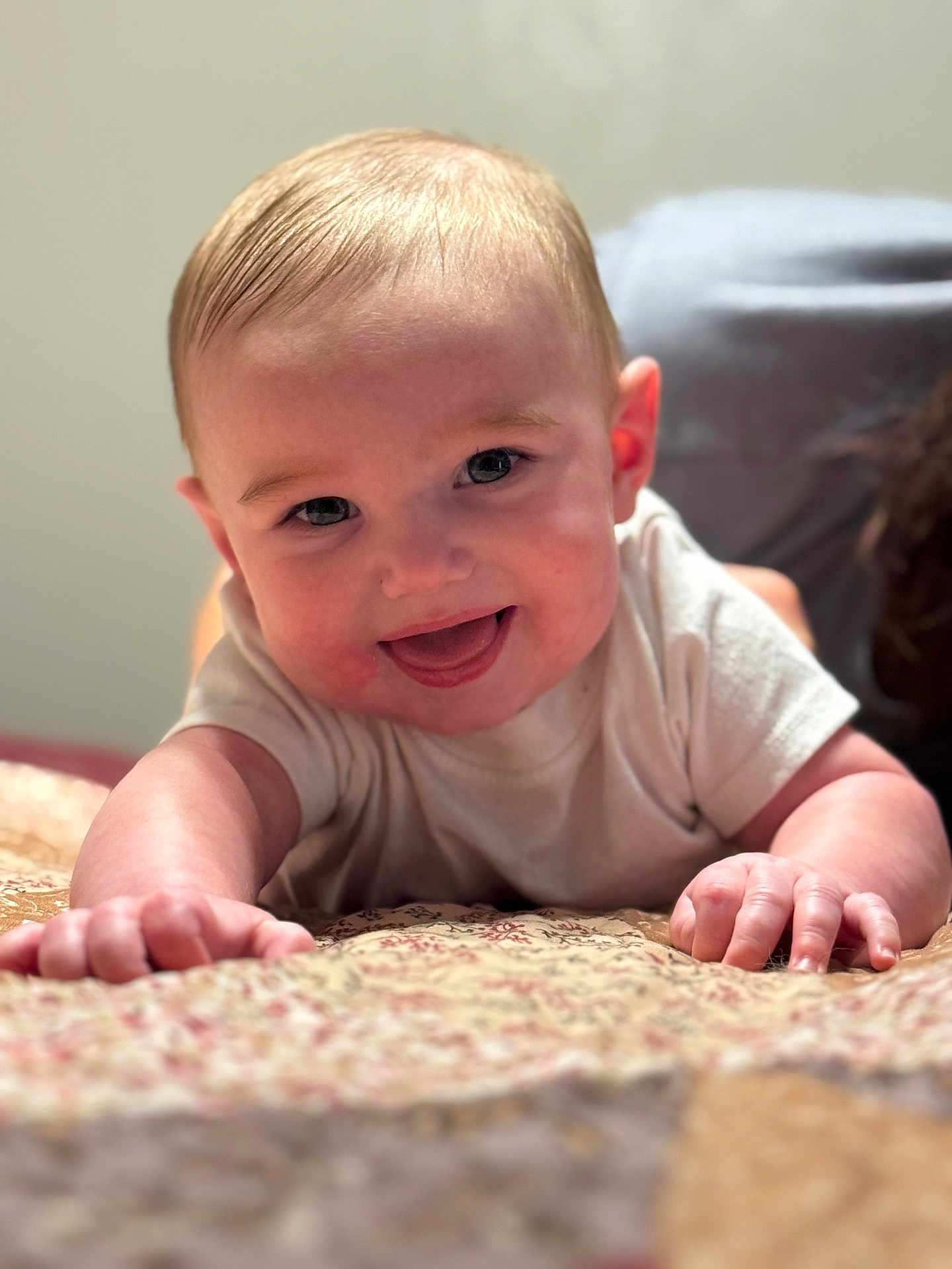 Tate is registered to the contest to win money with this photo: baby, smiling, infant, face, hands, blanket, pattern, happy, cute, person, skin, closeup, portrait, indoors, toddler, crawling, young_child, soft_light, expression, casual_clothing