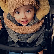 Thiago participe au concours pour gagner de l'argent avec cette photo : toddler, child, smiling, hat, hood, jacket, stroller, blue_jeans, cozy, winter_clothing, happy, cute, baby, face, eyes, hands, seated, warm, outerwear, portrait