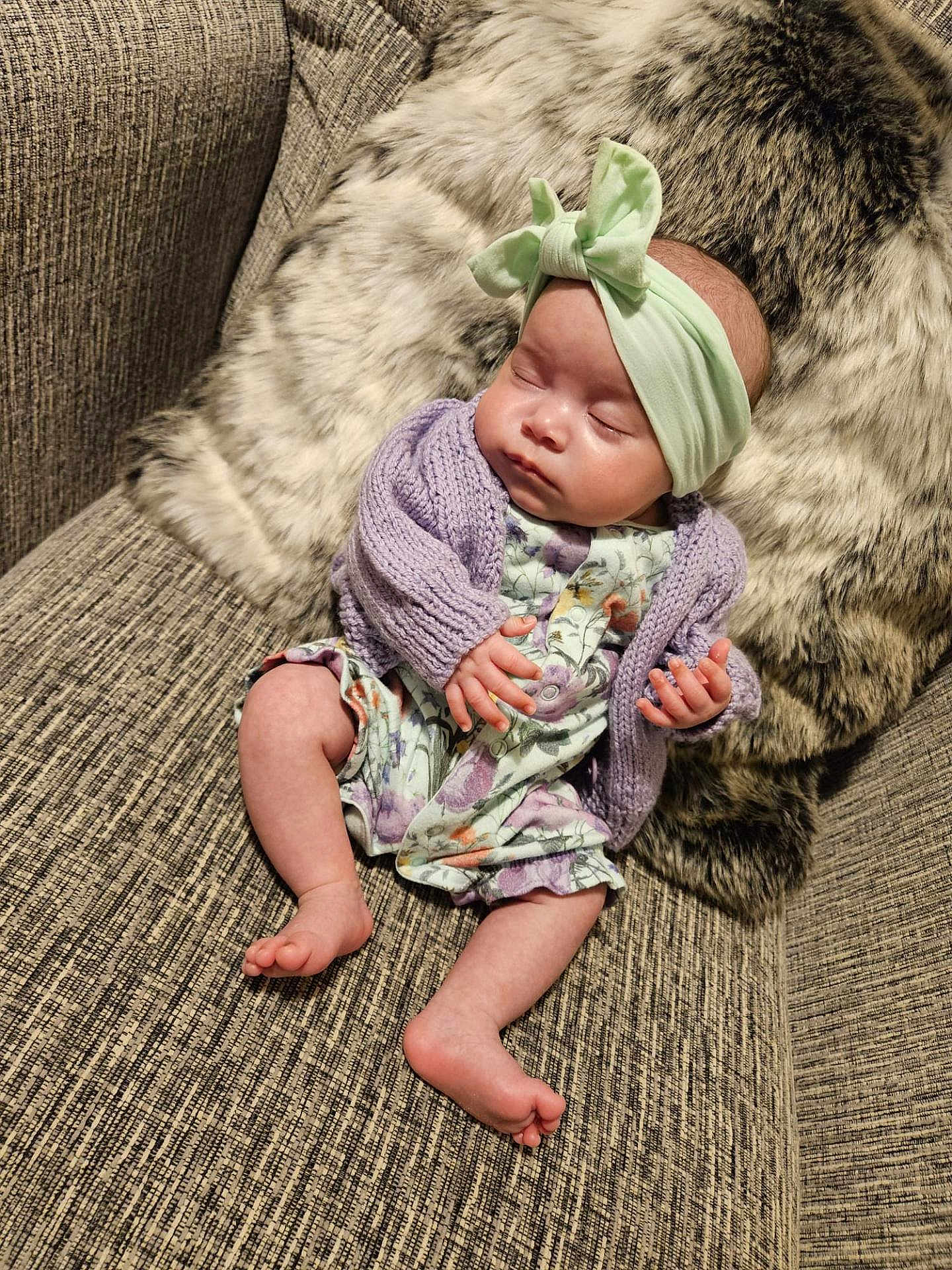 Kyla-Faith is registered to the contest to win money with this photo: baby, sleeping, infant, headband, bow, purple_cardigan, floral_outfit, couch, furry_pillow, cozy, indoor, person, cute, peaceful, relaxed, small_hands, bare_feet, texture, soft, rest