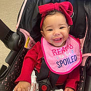 Sinayah is registered to the contest to win money with this photo: baby, baby_girl, car_seat, child, clothing, cute, face, floral_pants, happy, headband, indoors, infant, person, pink_bib, red_bow, red_outfit, seatbelt, sitting, smiling, stroller