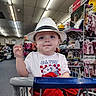 baby, child, shopping_cart, hat, fedora, clothing, store, retail, indoor, portrait, cute, blue_eyes, smile, infant, rack, baby_clothes, shopping, casual_wear, person, curious