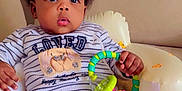 Charlene is registered to the contest to win money with this photo: baby, child, comfort, couch, curly_hair, cute, expression, face, furniture, hand, indoor, infant, onesie, portrait, rattle, relaxing, seat, sitting, striped_clothing, toy